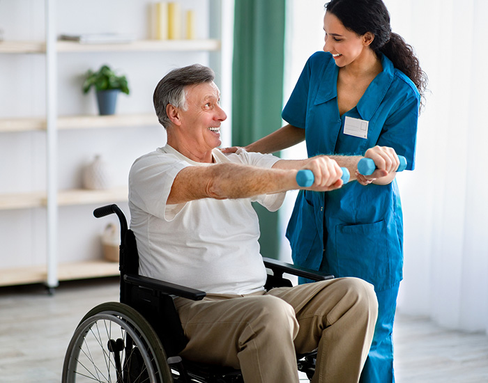 Female physiotherapist helping elderly man in wheelchair do exercises